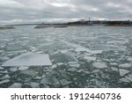 Broken sheets and pieces of ice float on the surface of Lake Michigan with a bridge in the distance in Milwaukee Wisconsin