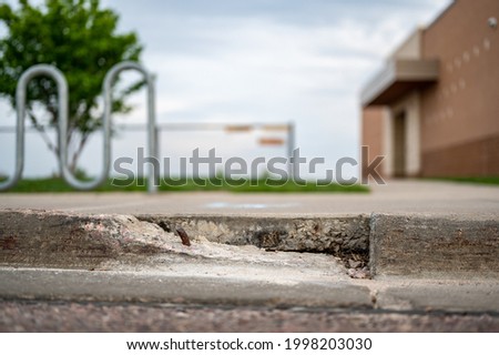 Broken sidewalk curb with exposed rebar and jagged edges that could cause a tripping hazard