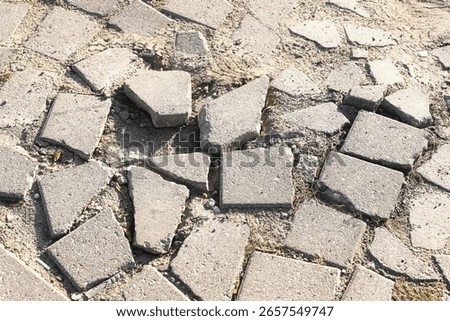 Broken sidewalk pavement surface. Damaged concrete tiles. Cracked footpath with sand. Uneven ground with rubble. Urban infrastructure problem. Dangerous surface for pedestrians. Street under repair.