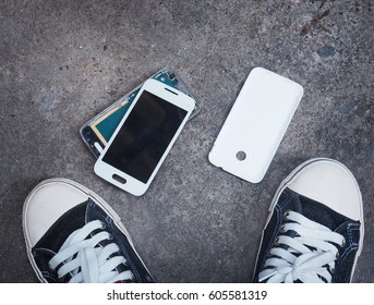 Broken Smart Phone After Being Dropped On Concrete Grunge Floor Between Owner's Sneaker Shoes 