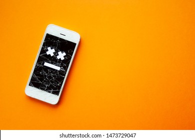 Broken smartphone with cracked destroyed screen on orange background with sad smile. Broken phone service, recovery and repair concept, symbol top view copyspace.