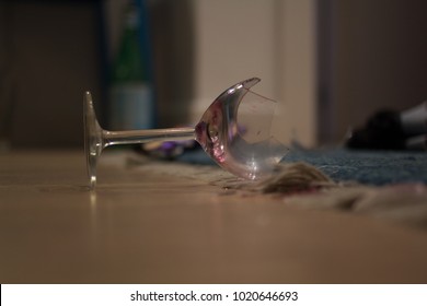A broken smashed wine glass on the floor late in the evening, representing the concept of drunkenness, debauchery, accident, and fragility.