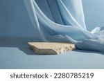 A broken stone podium displayed on a light blue background, decorated with a luxurious fabric. Empty space for cosmetic product presentation