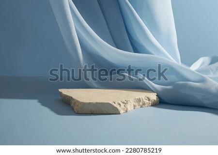 A broken stone podium displayed on a light blue background, decorated with a luxurious fabric. Empty space for cosmetic product presentation