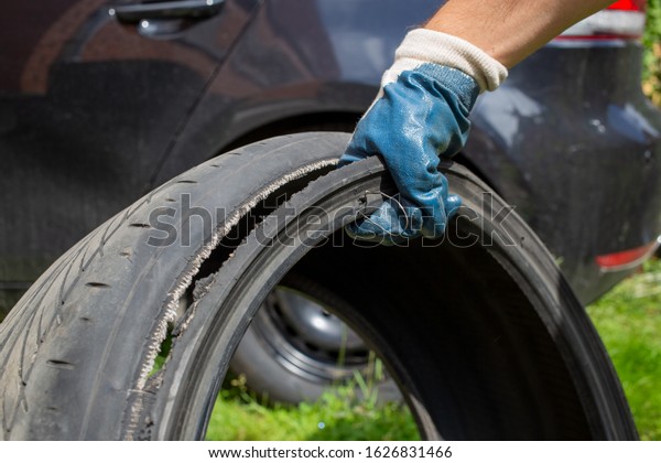 broken wheel.  the hand of the master in a blue\
glove holds the torn tire with wire. close up. on the background\
black car in blur