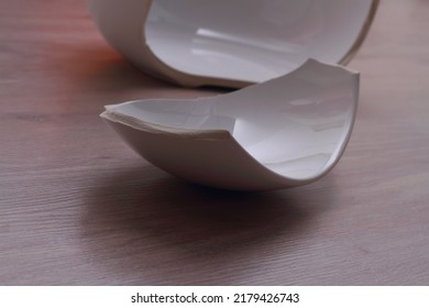 A Broken White Bowl On The Wooden Floor. Two Pieces And Edge