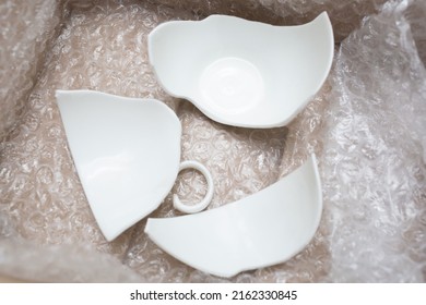 Broken white cup during transport in a box with bubble wrap for shipping. Flat lay. Top view. Concept of careless transportation of things. Close-up.
