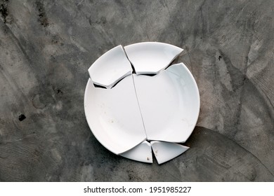 Broken White Plate, Pieces Of Shattered Dish On Raw Concrete Floor