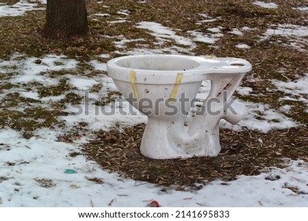 Broken white toilet bowl with paper tape on the lawn in the yard with snow.
