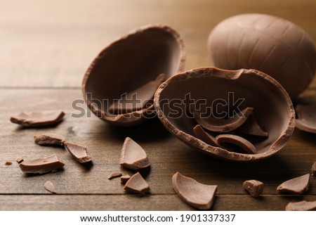Broken and whole chocolate egg on wooden table, closeup