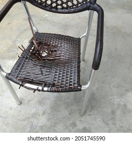 Broken Wicker Chair. The Webbing Started To Break And Bore A Hole In The Center Of The Chair. Outdoor Chair On Cement Background.