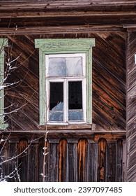The broken window of an abandoned wooden house. Interesting wooden paneling of the house. Alienation, abandonment is a distant point.