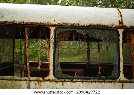 broken window of an old rusty school bus covered in moss, wet after rain