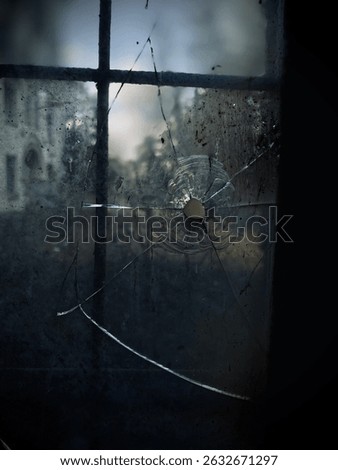 Broken window revealing a web and distant landscape in an abandoned setting at dusk