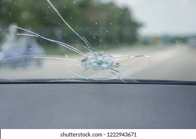 The broken windshield of the car from flying stone. The hole in the glass, chips and debris, cracks in strips. The glass reflects the sky with clouds.