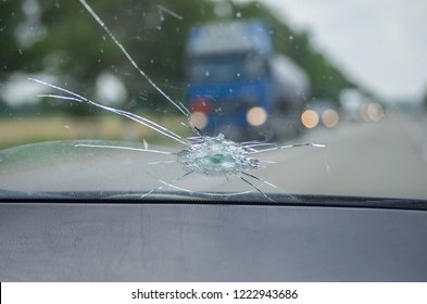 The broken windshield of the car from flying stone. The hole in the glass, chips and debris, cracks in strips. The glass reflects the sky with clouds.