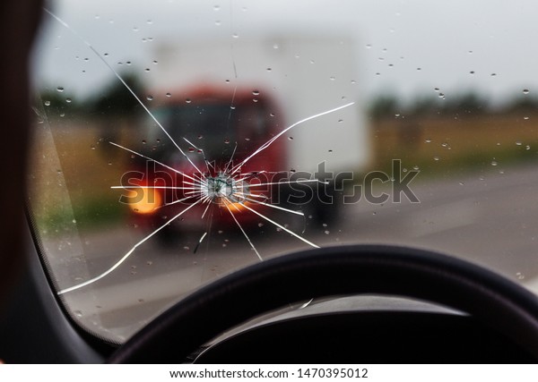 Broken windshield of a car. A web of radial splits,\
cracks on the triplex windshield. Broken car windshield, damaged\
glass with traces of oncoming stone on road or from bullet trace in\
car glass