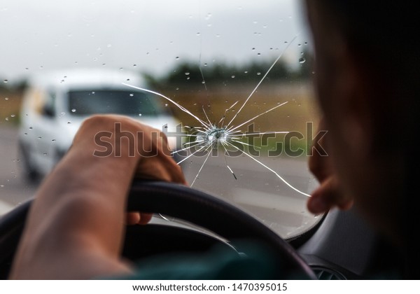 Broken windshield of a car. A web of radial splits,\
cracks on the triplex windshield. Broken car windshield, damaged\
glass with traces of oncoming stone on road or from bullet trace in\
car glass