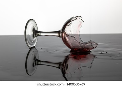 Broken wine glass with red wine which is laying on the wet surface. White background - Powered by Shutterstock