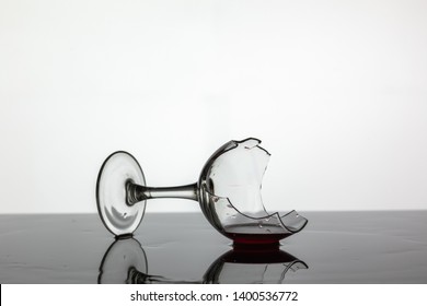 Broken wine glass with red wine which is laying on the wet surface. White background - Powered by Shutterstock