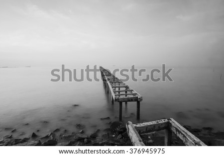 Broken wood bridge and waves crashing on sea in black and white mode