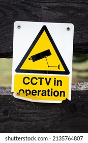 Broken yellow cctv in operation warning sign on a wooden fence