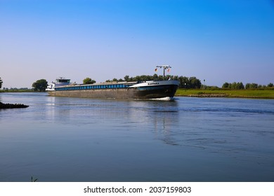 Bronkhorst, Netherlands - July 9. 2021: View on inland waterway vessel cargo ship on river Ijssel in rural dutch landscape against blue summer sky (focus on ship)