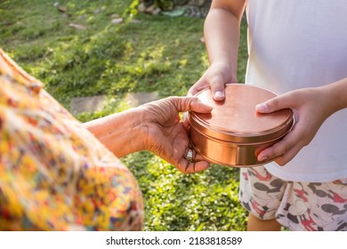 A Bronze Aluminum Tin Can With A Cake Inside Is Handed Over From An Old Person To Her Grandchild Graciously.