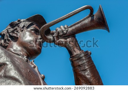 Bronze cast statue with brown patina of an American Civil War soldier playing the bugle.