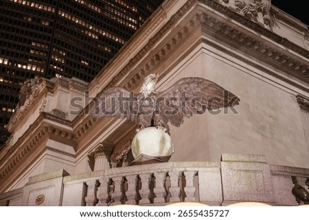 A bronze eagle statue with spread wings stands above the entrance of Grand Central Terminal in New York City. The historic architectural details and surrounding buildings frame the scene beautifully