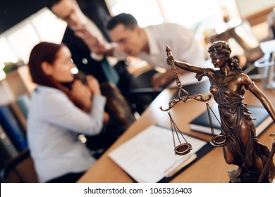 Bronze figurine of Themis holds wedding rings on scales of balance, being in foreground. Couple divorce. Adult couple gets divorced from attorney for divorce in office.