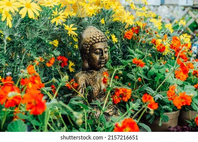 Bronze Gautama Buddha decorative statue in a garden with red and yellow flowers. Exterior, Outdoor Garden decor concept. Selective focus.