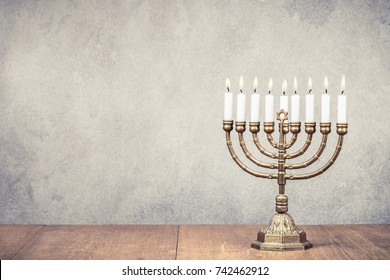 Bronze Hanukkah menorah with burning candles on wooden table front old vintage concrete wall background. Holiday greeting card concept. Retro instagram style filtered photo
