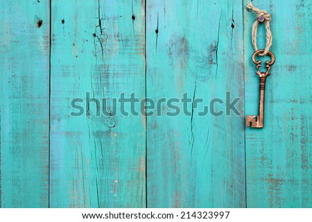 Bronze skeleton house key hanging by rope on blank antique teal blue rustic wood door; real estate background with wooden painted copy space