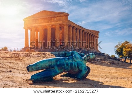 Bronze statue of Icarus in front of the Temple of Concordia at the Valley of the Temples. Temple of Concordia and the statue of Fallen Icarus, in the Valley of the Temples, Agrigento, Sicily, Italy.