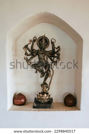 A bronze statue of the Indian goddess druga stands in the alcove of a white wall in a yoga studio