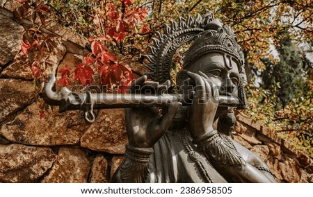 Bronze statue of Lord Krishna playing on flute. Autumn nature. Hinduism religion