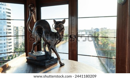 Bronze statue of scientist cat with glasses standing on books and holding keys on tail in upper room of decorative lighthouse in Fishing village, Kaliningrad, Russia. Embankment of Pregolya River.