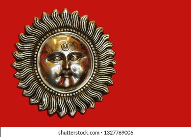 Bronze sun with a face and a mustache on a red background. Surya.