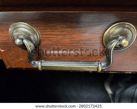 Bronze worn drawer handle on a dark oak wood drawer.