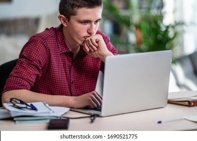 Brooding Active Teen Guy With Headphones Listens To Lecture, Does In Notebook, Using Laptop And Makes Notes In Notepad. Concept Of Online Learning. Social Distance, Self-isolation. Distance Learning.