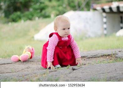 Brooding Baby Girl Squatting Outdoors With A Doll