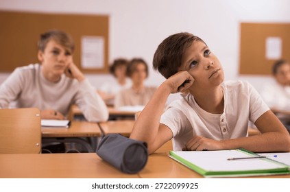 Brooding boy stands in a school class against the background of classmates
