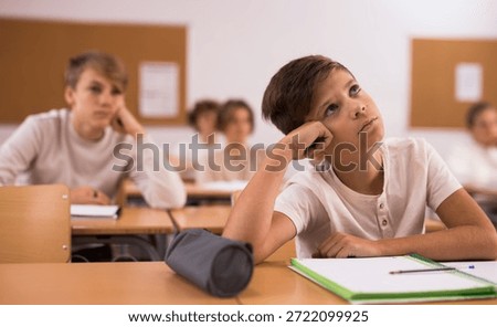 Brooding boy stands in a school class against the background of classmates