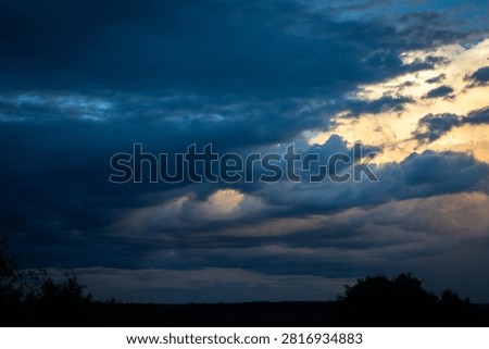 Brooding clouds gather over a quiet horizon with pale light breaking through layered textures suggesting passing showers and unsettled conditions during a tranquil summer twilight