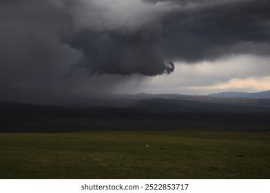 Brooding clouds leak rain as a summer storm breaks over the grasslands near Lake Song-Kul, Kyrgyzstan 