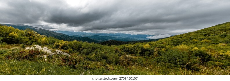 Brooding clouds sweeping over the Blue Ridge Mountains with lush early-autumn foliage and a wide valley unfolding in the distance.