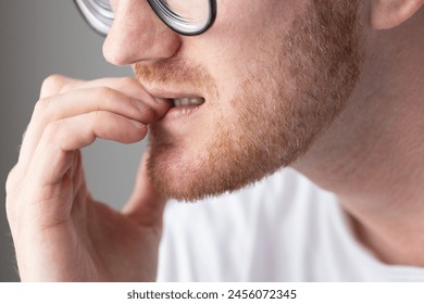 Brooding man in glasses chewing on his fingernails. Fingernail biting.
