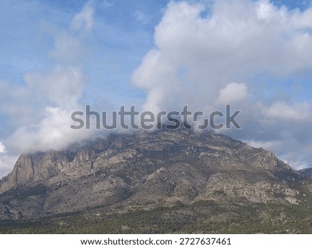 brooding mountain capped by clouds, dark ridgelines and voluminous cloud plumes spilling over summit, textured