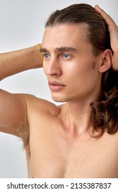 Brooding shirtless man looking at side and touching hair isolated over white background. Young caucasian guy with long hair posing at camera, looking thoughtful and pacified, calm